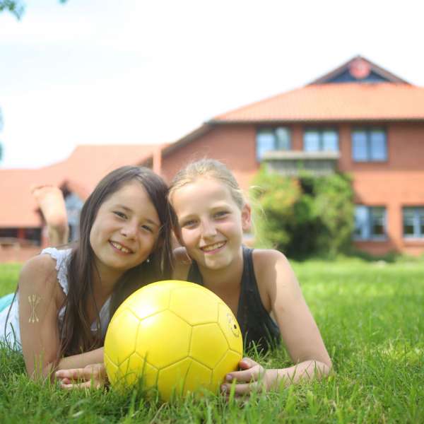 To piger ligger i græsset med en fodbold i hænderne på vandrehjemmet i Tønning.